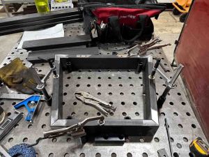 A frame made of rectangular steel tube is fixtured to the fixture table with clamps and blocks.